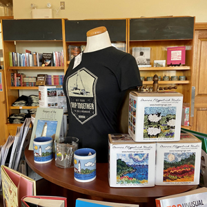 Museum gift shop featuring "Get Your Ship Together" T-shirt in black, and other items.