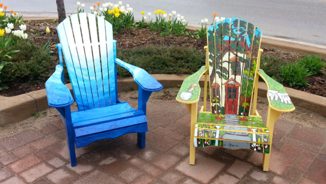 Two Adirondack chairs are displayed outdoors on a brick patio, they are hand painted.