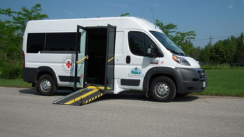 A white accessible transit van with a deployed ramp and the Red Cross and Town of Collingwood logos on the side.