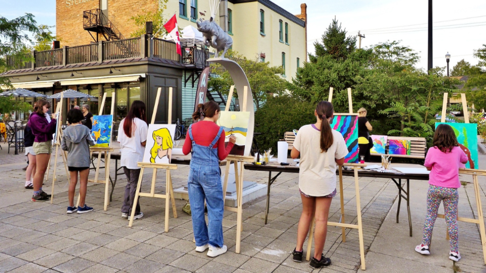 Several people are painting on easels outdoors in front of a brick building.