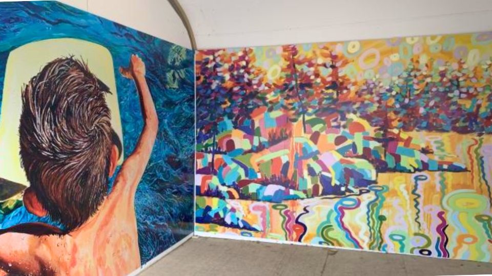 A mural featuring a person from behind reaching into a bright light, and a colorful abstract landscape with trees and water.