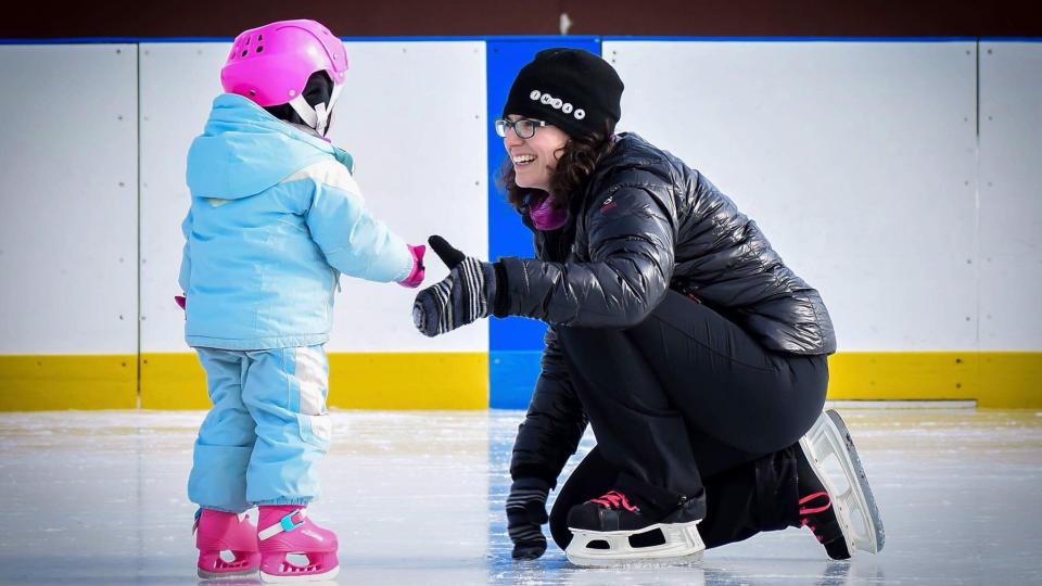 Mom kneeling smiling at daughter in skates outdoor rink