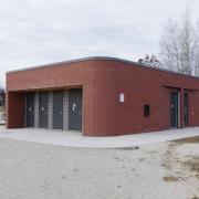 A rectangular brick building with four black doors on the front and one on the side