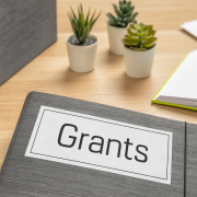 binder labeled grants on a light wood desk with decorative succulents