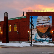 A large mural of the stern of a cargo ship is painted on the side of a red brick building.