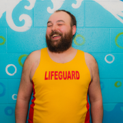 A person wearing a yellow and red lifeguard tank top laughs
