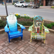 Two Adirondack chairs are displayed on a brick sidewalk.