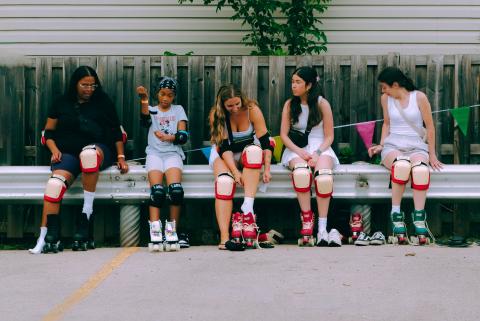 Girls lacing up roller skates wearing red and white knee pads