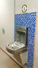 Metal water fountain on a wall with blue checkered tiles