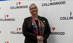 A woman stands smiling in front of an "I heart Collingwood" backdrop